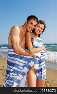 Young couple on beach wrapped in towel, portrait