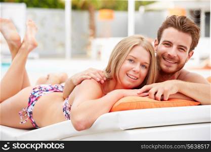 Young Couple On Holiday Relaxing By Swimming Pool
