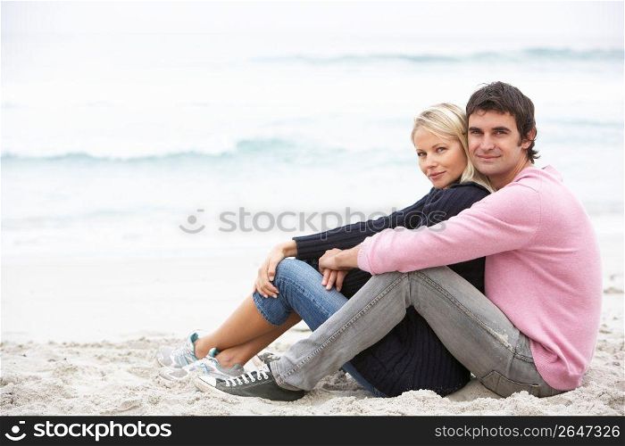 Young Couple On Holiday Sitting On Winter Beach