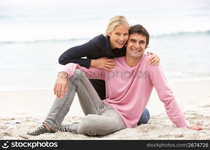 Young Couple On Holiday Sitting On Winter Beach