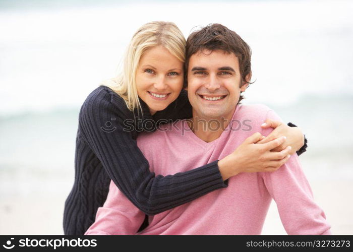 Young Couple On Holiday Sitting On Winter Beach