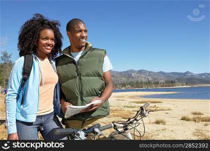 Young Couple on Mountain Bikes Using Map by lake