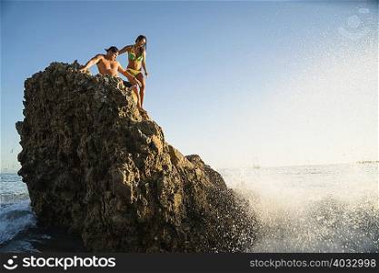 Young couple on rock with waves splashing at Newport Beach, California, USA