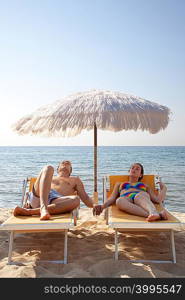 Young couple on sun loungers holding hands