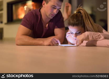 Young Couple on the floor in front of fireplace surfing internet using digital tablet on cold winter night