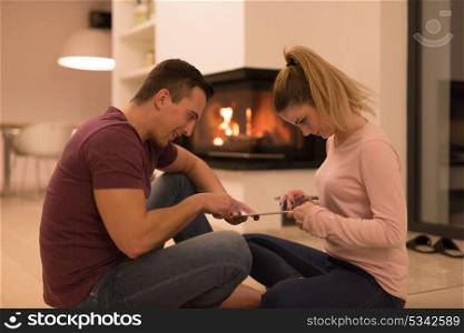 Young Couple on the floor in front of fireplace surfing internet using digital tablet on cold winter night