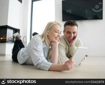 Young Couple on the floor in front of fireplace surfing internet using digital tablet on cold winter day