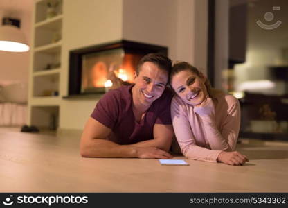 Young Couple on the floor in front of fireplace surfing internet using digital tablet on cold winter night