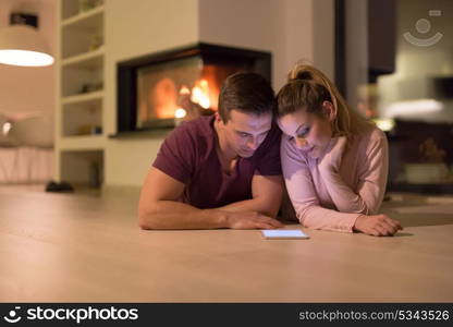 Young Couple on the floor in front of fireplace surfing internet using digital tablet on cold winter night