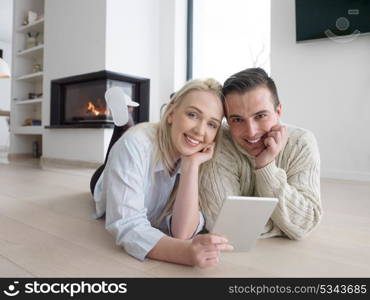 Young Couple on the floor in front of fireplace surfing internet using digital tablet on cold winter day