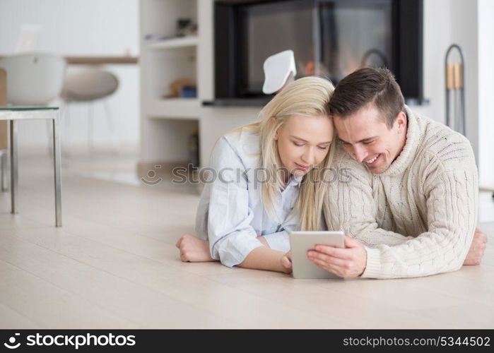 Young Couple on the floor in front of fireplace surfing internet using digital tablet on cold winter day