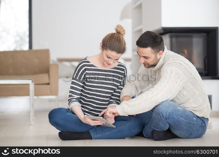 Young Couple on the floor in front of fireplace surfing internet using digital tablet on cold winter day