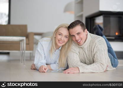 Young Couple on the floor in front of fireplace surfing internet using digital tablet on cold winter day