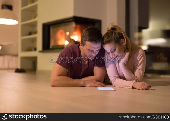 Young Couple on the floor in front of fireplace surfing internet using digital tablet on cold winter night