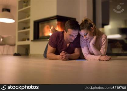 Young Couple on the floor in front of fireplace surfing internet using digital tablet on cold winter night