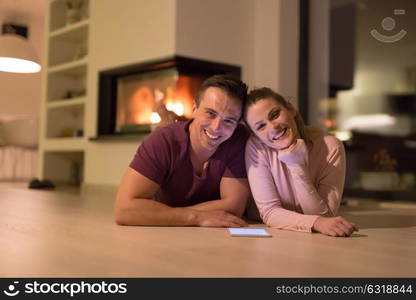 Young Couple on the floor in front of fireplace surfing internet using digital tablet on cold winter night