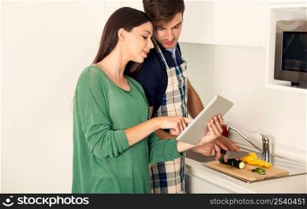 Young couple on the kitchen follow a recipe by tablet and cooking