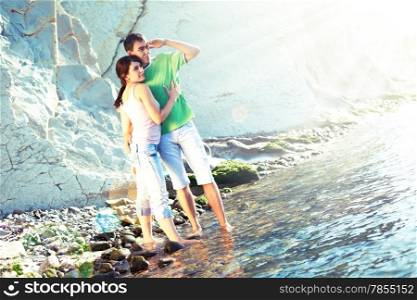 Young couple on the rocky coast standing ankle-deep in water and looking over the horizon