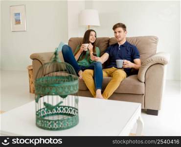 Young couple on the sofa drinking coffee while watching tv