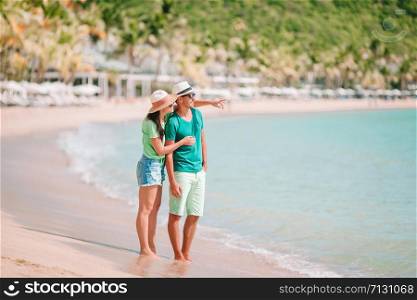 Young couple on white beach during summer vacation. Happy lovers enjoy their honeymoon at exotic island. Young couple walking on tropical beach with white sand and turquoise ocean water at Antigua island in Caribbean