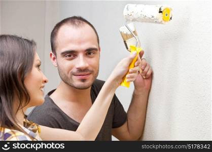 Young couple painting a wall with roller and doing repair at home together