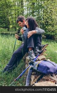 Young couple pausing to eat and drink while doing trekking outdoors. Couple pausing while doing trekking