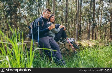 Young couple pausing to eat and drink while doing trekking outdoors enjoying nature. Couple pausing while doing trekking