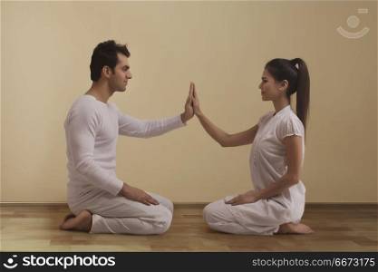 Young couple performing yoga face to face touching hands