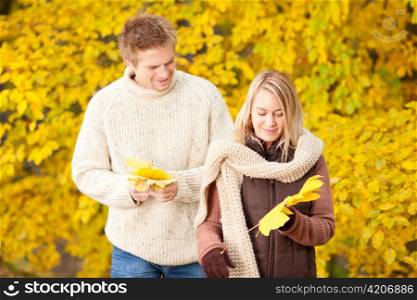 Young couple picking leaves in autumn park outfit
