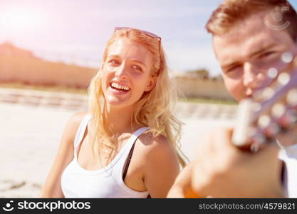 Young couple playing guitar on beach in love. Happy romantic young couple playing guitar on beach in love