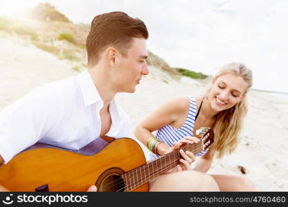 Young couple playing guitar on beach in love. Happy romantic young couple playing guitar on beach in love