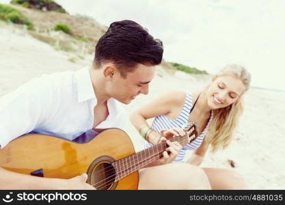 Young couple playing guitar on beach in love. Happy romantic young couple playing guitar on beach in love