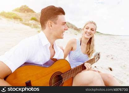 Young couple playing guitar on beach in love. Happy romantic young couple playing guitar on beach in love