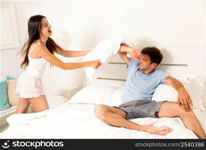 Young couple playing the bed and fighting with pillows