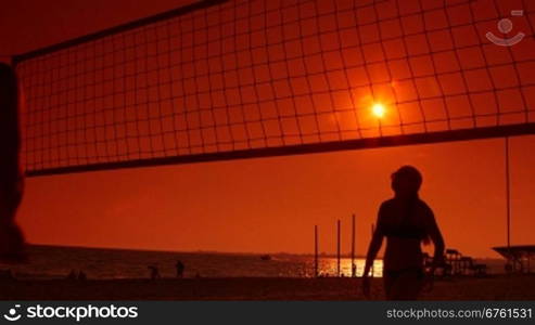 Young couple playing volleyball on summer beach at sunset