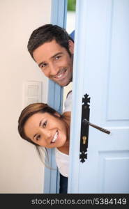 Young couple poking their heads around the front door