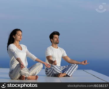 young couple practicing yoga at sunset in modern home terace with ocean and sunset in background