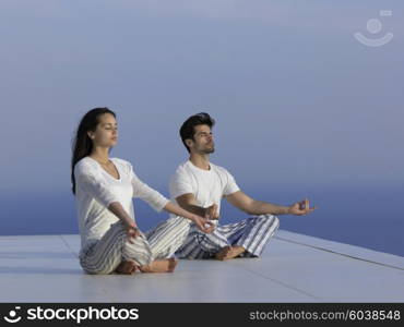 young couple practicing yoga at sunset in modern home terace with ocean and sunset in background