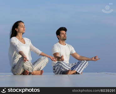 young couple practicing yoga at sunset in modern home terace with ocean and sunset in background