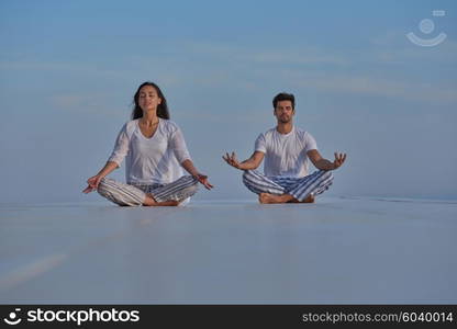 young couple practicing yoga at sunset in modern home terace with ocean and sunset in background