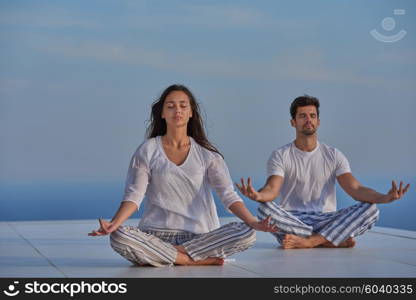 young couple practicing yoga at sunset in modern home terace with ocean and sunset in background