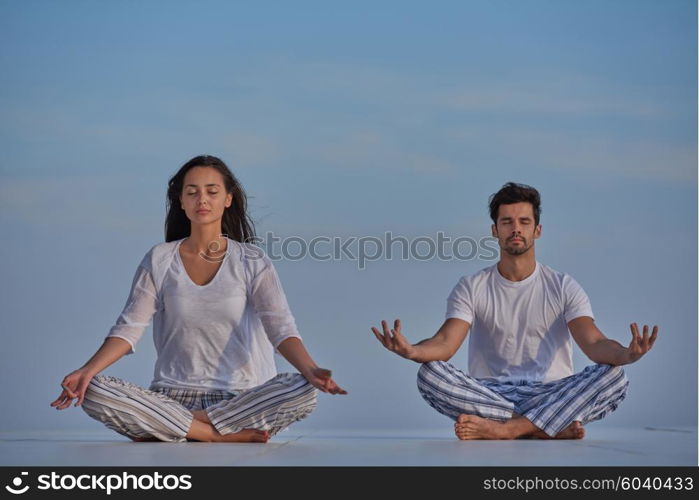 young couple practicing yoga at sunset in modern home terace with ocean and sunset in background