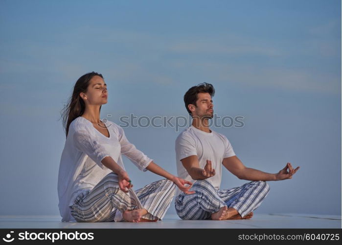 young couple practicing yoga at sunset in modern home terace with ocean and sunset in background