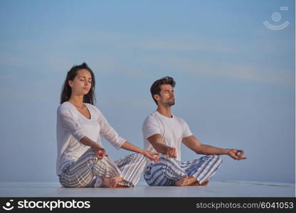 young couple practicing yoga at sunset in modern home terace with ocean and sunset in background