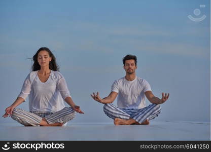 young couple practicing yoga at sunset in modern home terace with ocean and sunset in background