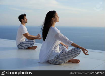 young couple practicing yoga at sunset in modern home terace with ocean and sunset in background