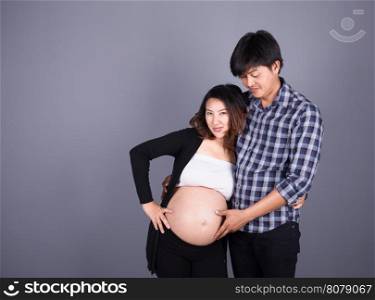 young couple: pregnant mother and happy father on gray wall background
