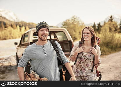 Young couple preparing to go hiking, carrying firewood, smiling
