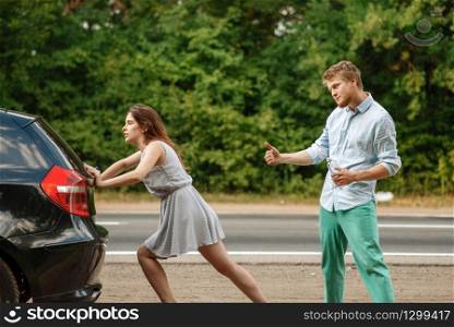 Young couple pushing broken car on road, breakdown. Crashed automobile or emergency accident with vehicle, trouble with engine on highway
