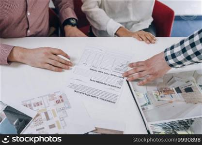 Young couple reading and preparing to sign mortgage contract in real estate agency office.. Real Estate Agency. Young Couple Signing Financing Contract